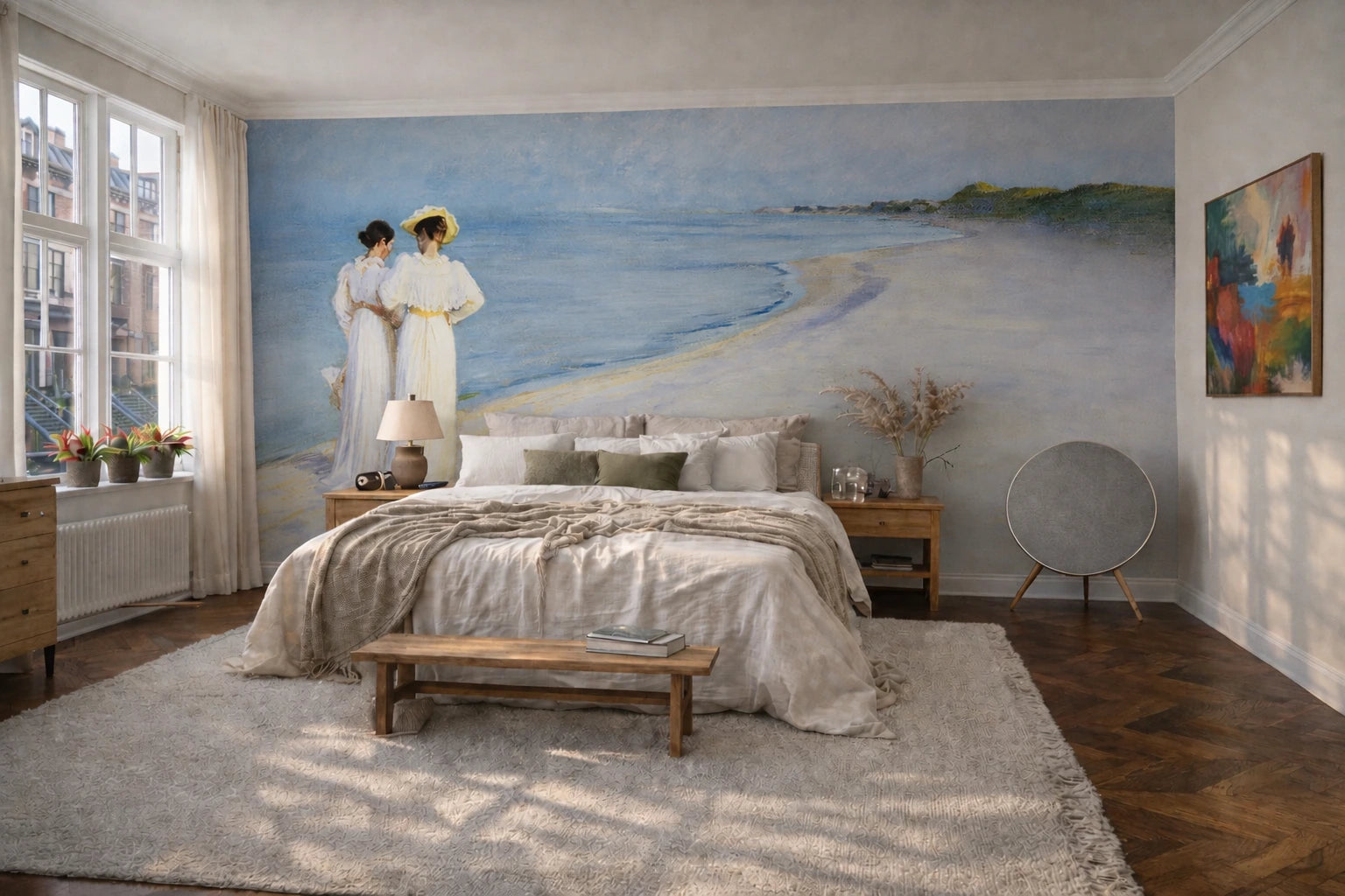 "Summer Evening on the Southern Beach" by Peder Severin Krøyer, made as a large wallpaper mural depicting a beach scene with two women in white dresses stands on the bedroom wall behind a bed with neutral bedding. The room has wood floors, a light rug, bedside tables, and a window on the left.