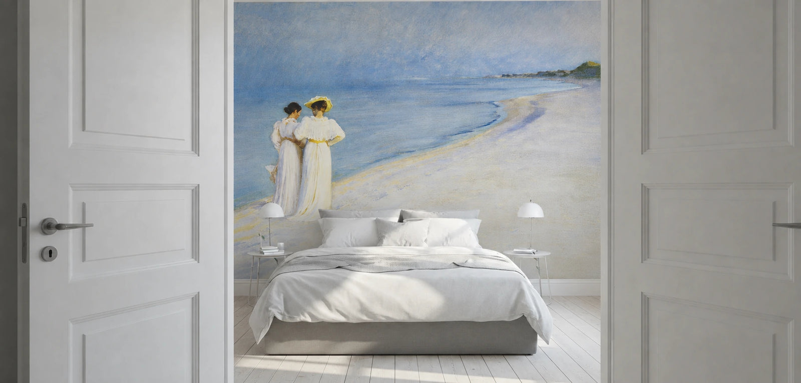 A large wall mural depicting "Summer Evening on the Southern Beach" by Peder Severin Krøyer, made as a large wallpaper mural. Featuring a beach scene with two figures in white robes, shown installed in a bedroom above a bed with white bedding and flanked by open white paneled doors.
