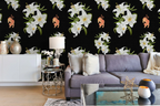 A styled living room featuring a black wallpaper with a repeating pattern of white lilies and small tigers, shown behind a purple sofa with decorative pillows and side tables.