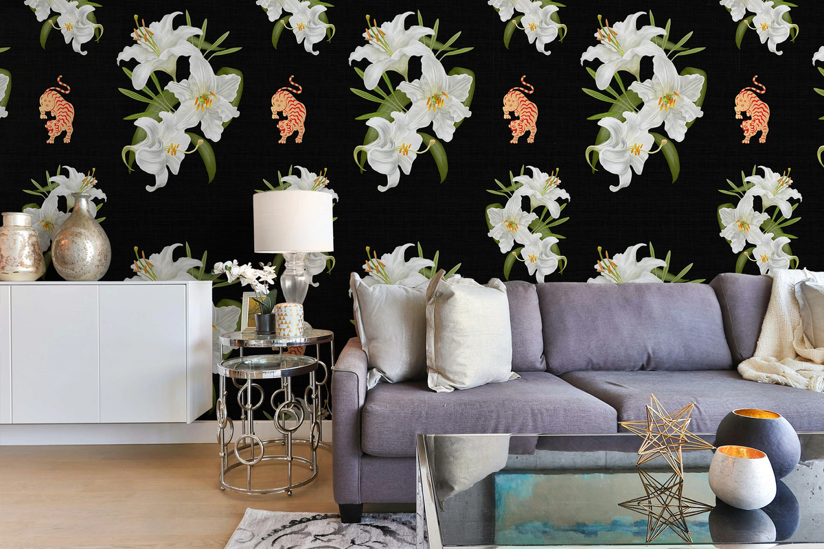 A styled living room featuring a black wallpaper with a repeating pattern of white lilies and small tigers, shown behind a purple sofa with decorative pillows and side tables.