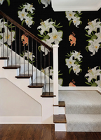 Staircase with wooden rail, white details, and a bold floral wallpaper pattern with lilies and tigers on a black background. 