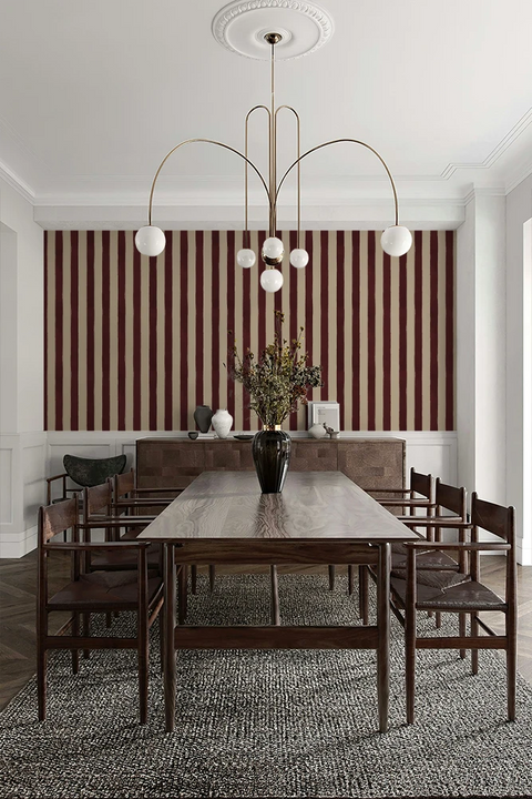 Dining room with a long table and chairs against a striped wallpaper.