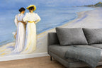 "Summer Evening on the Southern Beach" by Peder Severin Krøyer, made as a large wallpaper mural depicting a beach scene with two women in white dresses. Int front of the art mural is a grey sofa, on hardwood floors. 