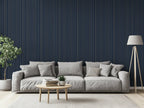 Modern living room with striped gold and navy wallpaper, a grey sofa, a lamp, and a plant. 