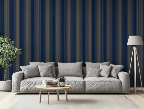 Modern living room with striped gold and navy wallpaper, a grey sofa, a lamp, and a plant. 