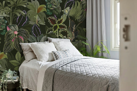 Bedroom with a bed against a wall featuring tropical leaf and flower wallpaper.