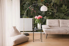 Modern living room with a sofa, lamp, and floral arrangement against a tropical wallpaper.