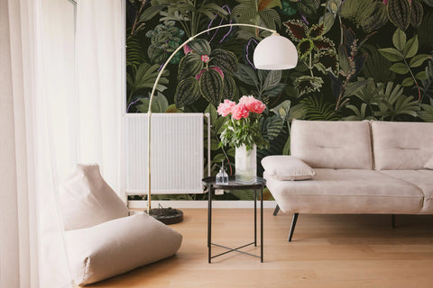 Modern living room with a sofa, lamp, and floral arrangement against a tropical wallpaper.