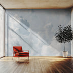 A big wallpaper mural showing a sky full of white clouds, seen in a lounge with a red chair and a tree. 