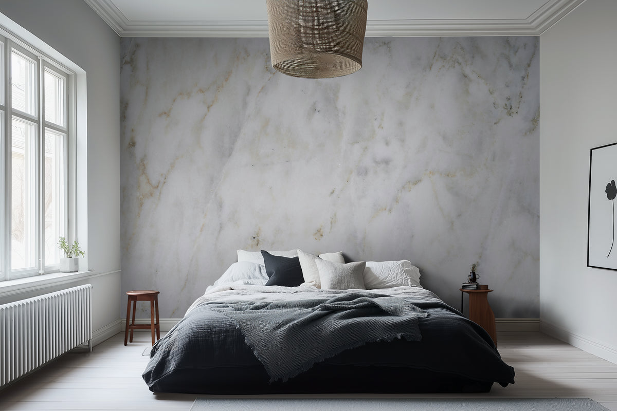 A bedroom with the Roma Cloud Marble wallpaper covering the wall behind the bed, featuring a creamy marble-like pattern with soft grey swirls.