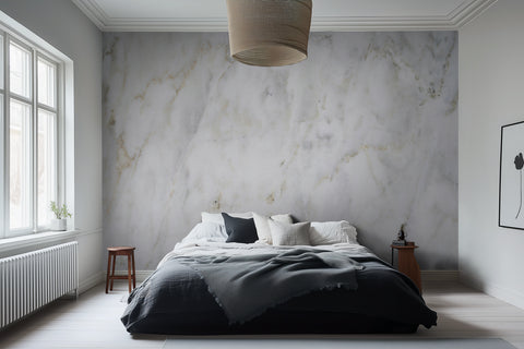 A bedroom with the Roma Cloud Marble wallpaper covering the wall behind the bed, featuring a creamy marble-like pattern with soft grey swirls.