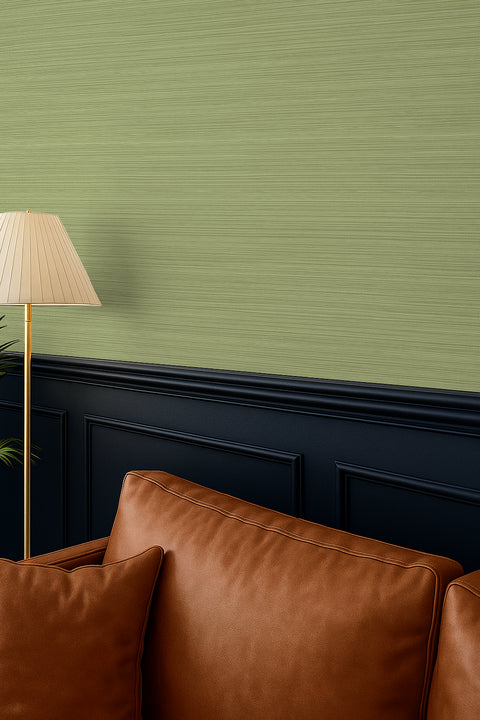 Brown leather sofa against a green wall with a lamp and green grasscloth wallpaper.