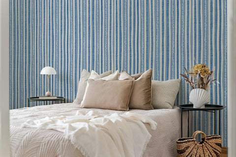 Bedroom with blue striped wallpaper, bed with beige pillows, and side tables.