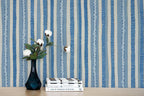 Stack of books with a vase and flowers against a blue and white striped wallpaper.