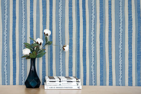 Stack of books with a vase and flowers against a blue and white striped wallpaper.