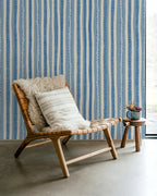 Wooden chair with patterned cushions against a blue and white striped wallpaper.