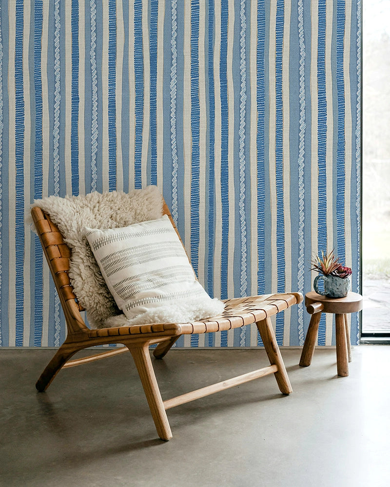 Wooden chair with patterned cushions against a blue and white striped wallpaper.
