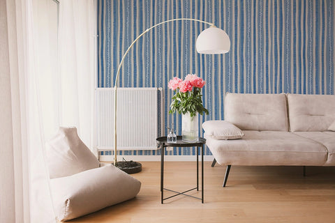 Modern living room with a beige sofa, armchair, and decorative lamp against a blue striped wallpaper.