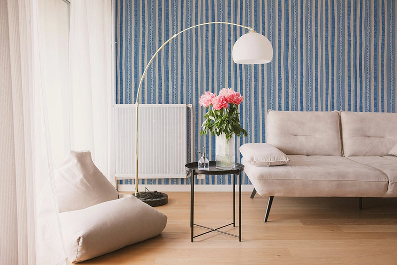 Modern living room with a beige sofa, armchair, and decorative lamp against a blue striped wallpaper.