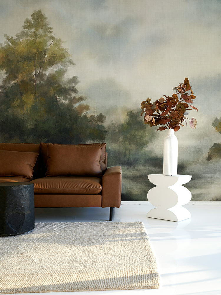 Modern living room with brown leather sofa, white side table, and nature-themed wallpaper mural.
