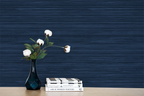 A flower on a desk, with books next to it. Navy blue faux grasscloth wallpaper with a rich woven texture.