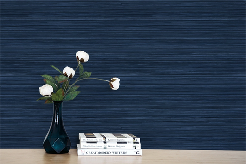 A flower on a desk, with books next to it. Navy blue faux grasscloth wallpaper with a rich woven texture.