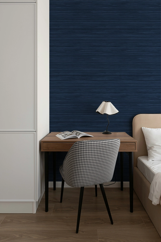 A small desk inside a modern bedroom, navy blue grasscloth wallpaper on the wall. 