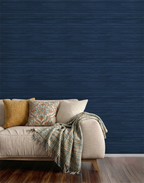 A living room with navy blue faux grasscloth wallpaper with a rich woven texture, a beige sofa with a blanket. 