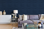 A modern maximalist living room with a blue sofa and navy blue faux grasscloth wallpaper with a rich woven texture. 