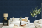 A modern maximalist living room with a beige sofa, olive tree, a and navy blue faux grasscloth wallpaper with a rich woven texture. 