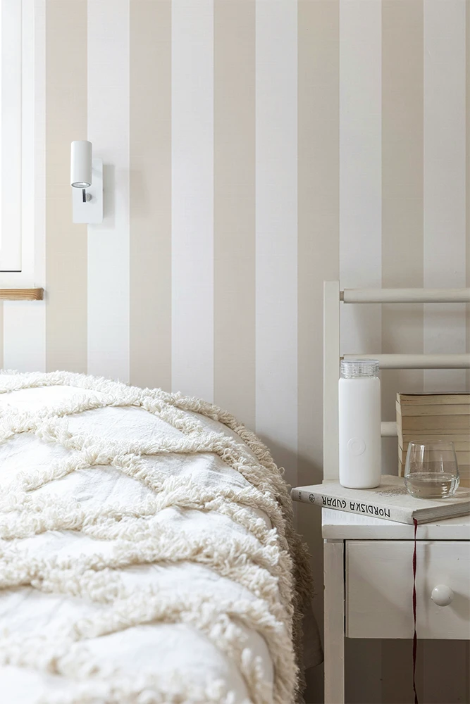 Bedroom with striped wallpaper, bed, nightstand, and lamp.