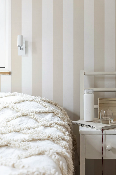Bedroom with striped wallpaper, bed, nightstand, and lamp.