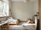 Nursery room with striped yellow wallpaper, wooden crib, and toys on a rug.