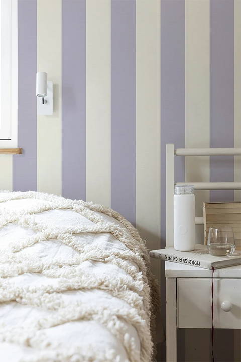 Room interior with striped purple wallpaper, bed, and side table.