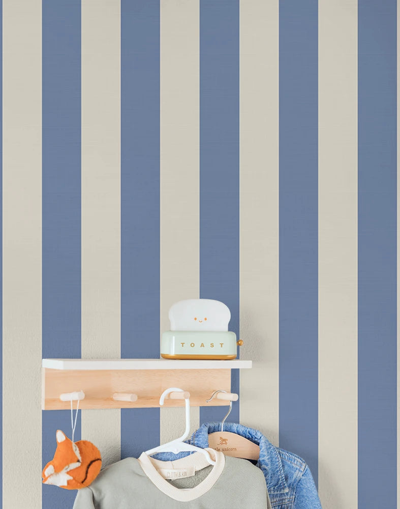 Wall with blue and beige striped wallpaper featuring a shelf and hanging kid's clothes.