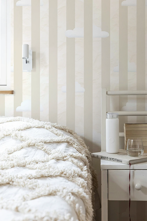 Bedroom with striped wallpaper, bed with white bedding, and nightstand with lamp.