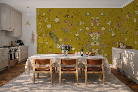 Kitchen with a dining table and chairs against a wall with chinoiserie wallpaper with a yellow background, featuring flowers and peacocks. 