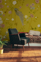 Room interior with a floral chinoiserie wallpapered wall, wicker chair, and patterned sofa.