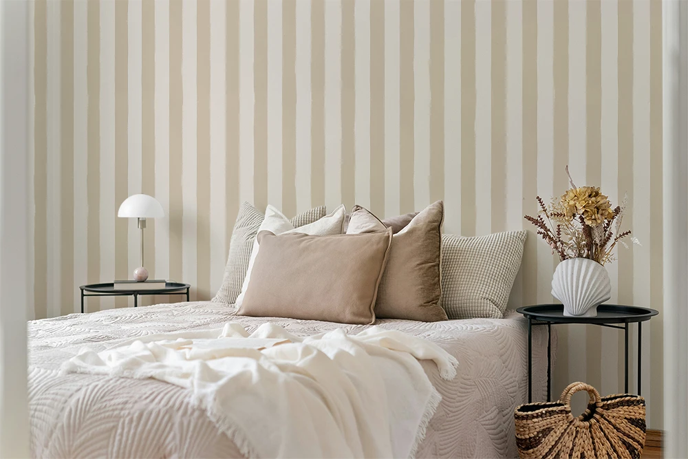 Neatly made bed with decorative pillows against a wall with beige a striped wallpaper.
