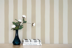 Vase with flowers and books on a wooden surface against a  wall with a beige striped wallpaper pattern.