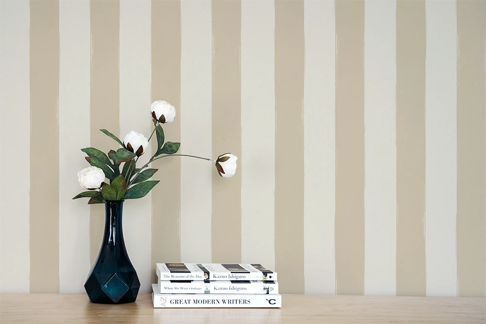 Vase with flowers and books on a wooden surface against a  wall with a beige striped wallpaper pattern.