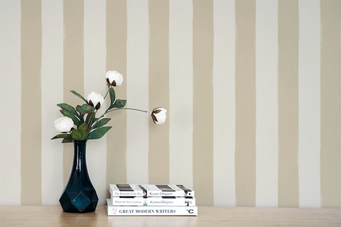 Vase with flowers and books on a wooden surface against a  wall with a beige striped wallpaper pattern.