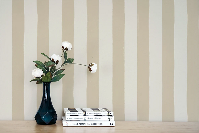 Vase with flowers and books on a wooden surface against a  wall with a beige striped wallpaper pattern.