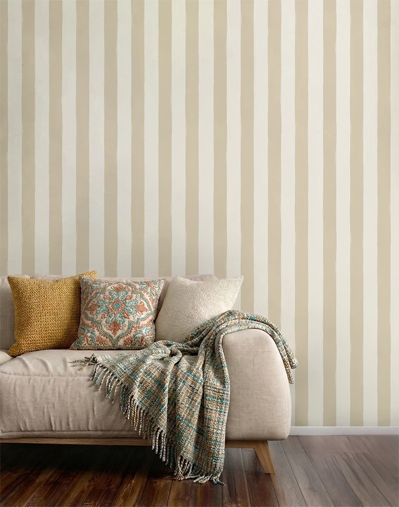 Beige sofa with decorative pillows and a blanket against a wall with a beige striped wallpaper pattern.