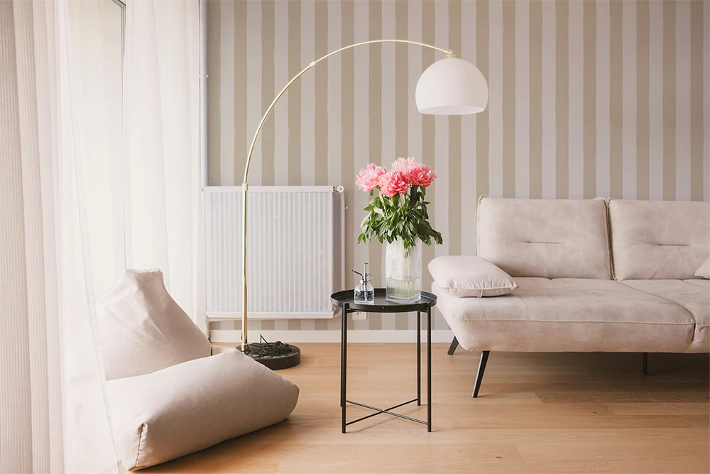 Modern living room with a beige sofa, armchair, a floor lamp and a wall with a beige striped wallpaper pattern.