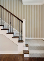 Staircase with wooden steps and metal railing against a wall with a beige striped wallpaper pattern.