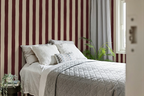 Bedroom with burgundy striped wallpaper, bed with white bedding, and a plant.