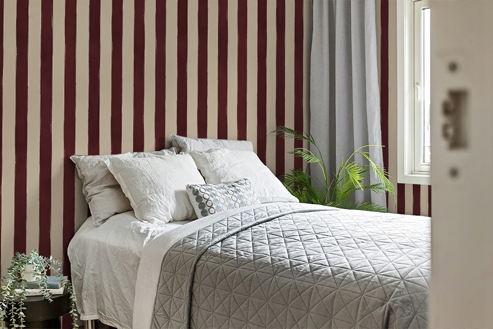 Bedroom with burgundy striped wallpaper, bed with white bedding, and a plant.