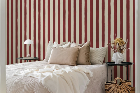 Bedroom with red and white striped wallpaper, bed with beige pillows, and side tables.