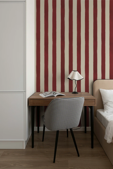 Small desk with lamp and chair against a red and white striped wallpaper.
